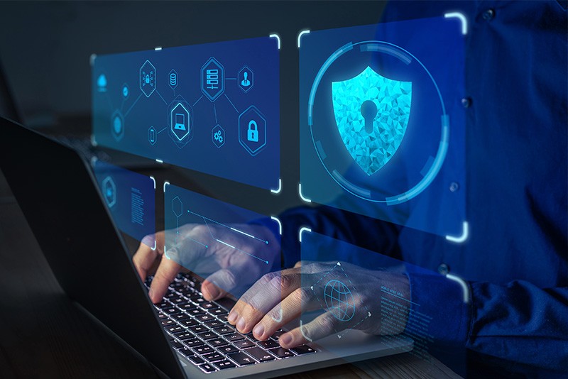 A man typing on a laptop with security icons on it.