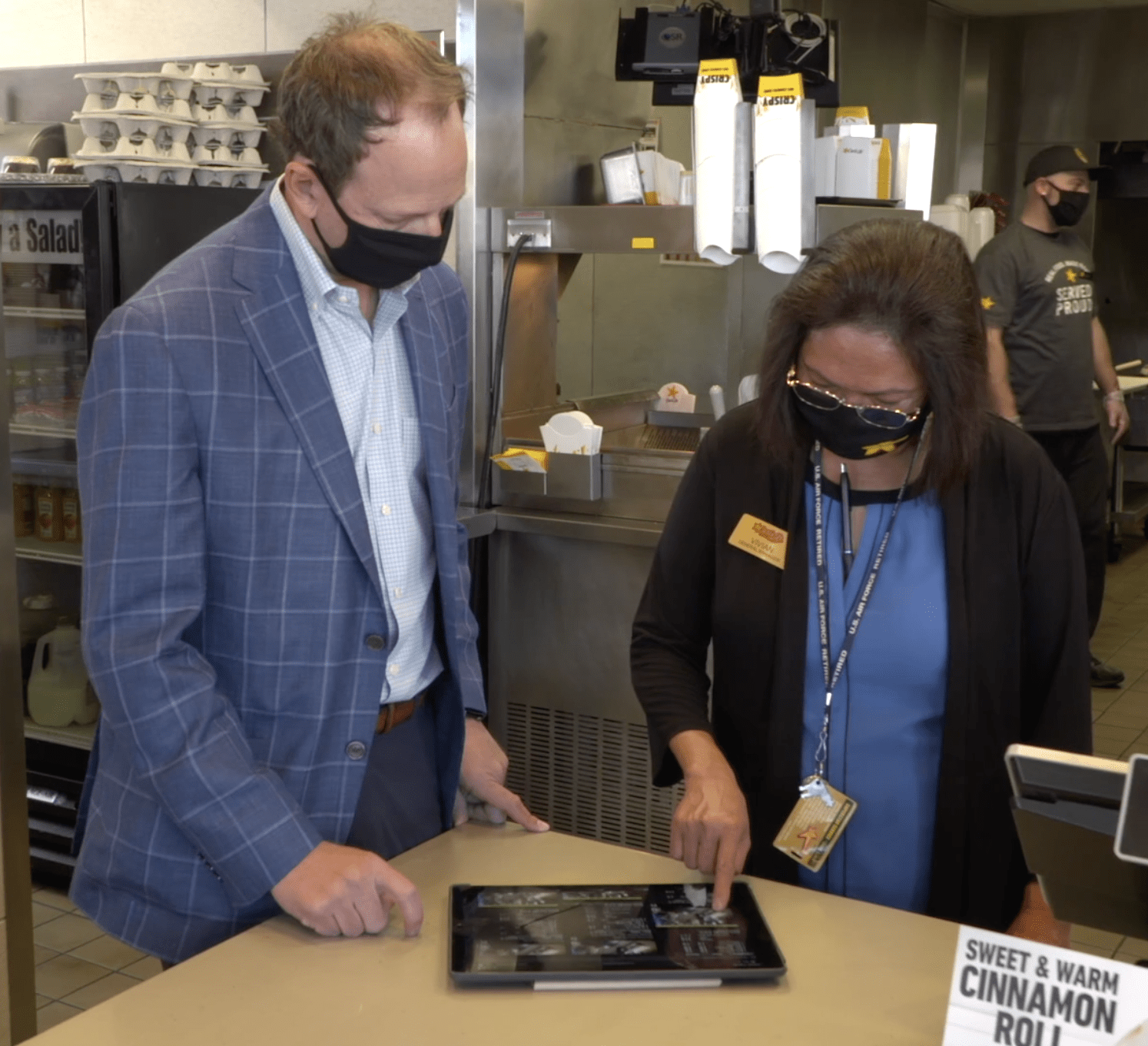 A man wearing a mask and a woman looking at a tablet.