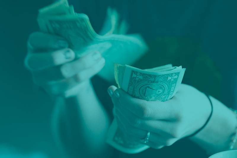 A person is holding money in front of a blue background.